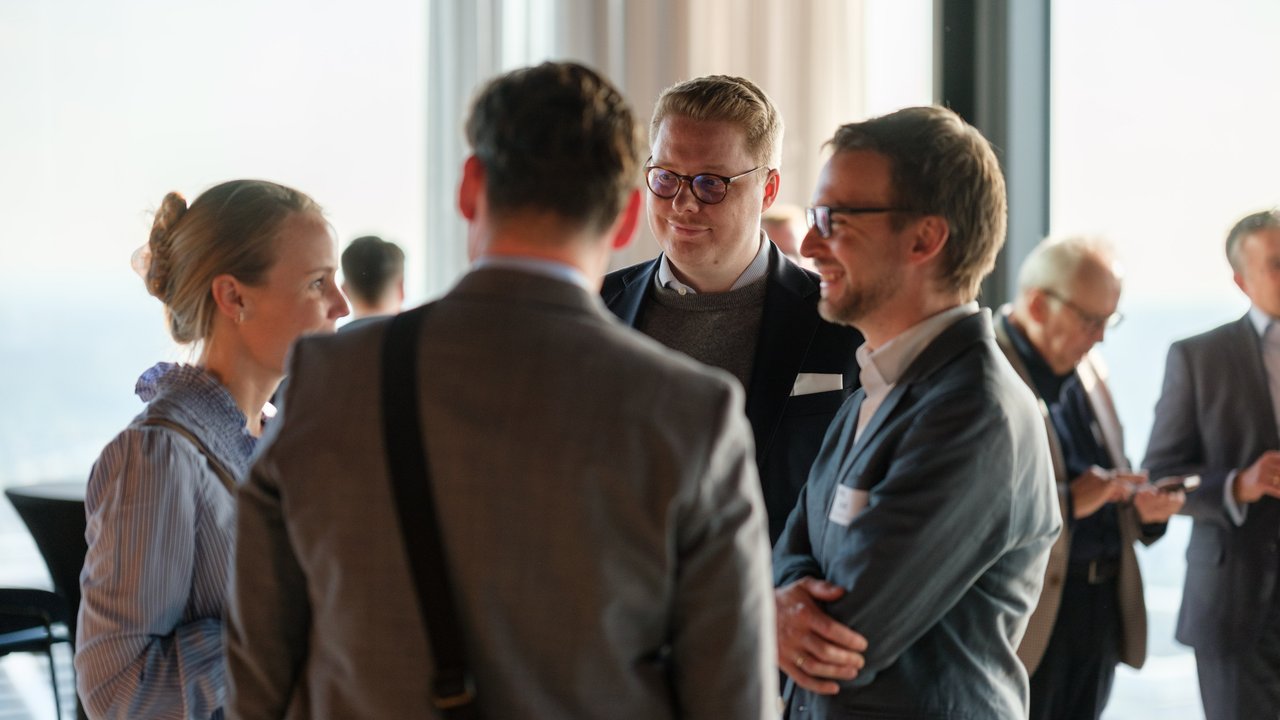 A group of four people engaged in conversation at a networking event, with a city view in the background.