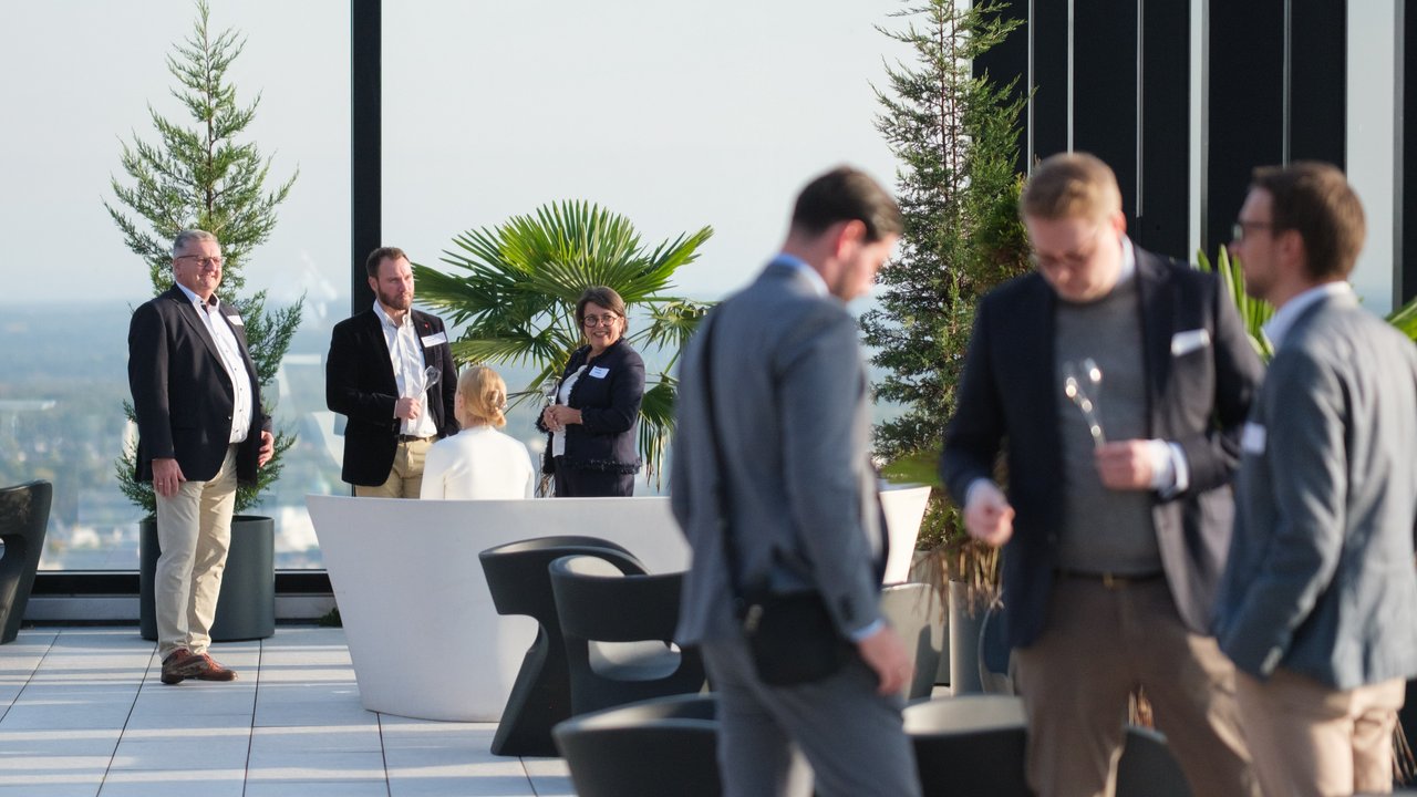 A group of people socializing on a rooftop terrace with plants and modern seating.