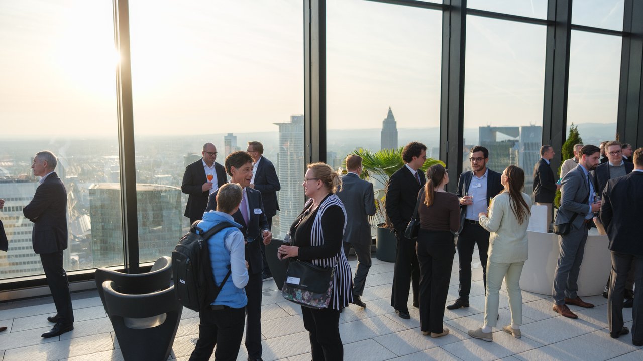 A group of professionals networking indoors with a city skyline view at sunset.