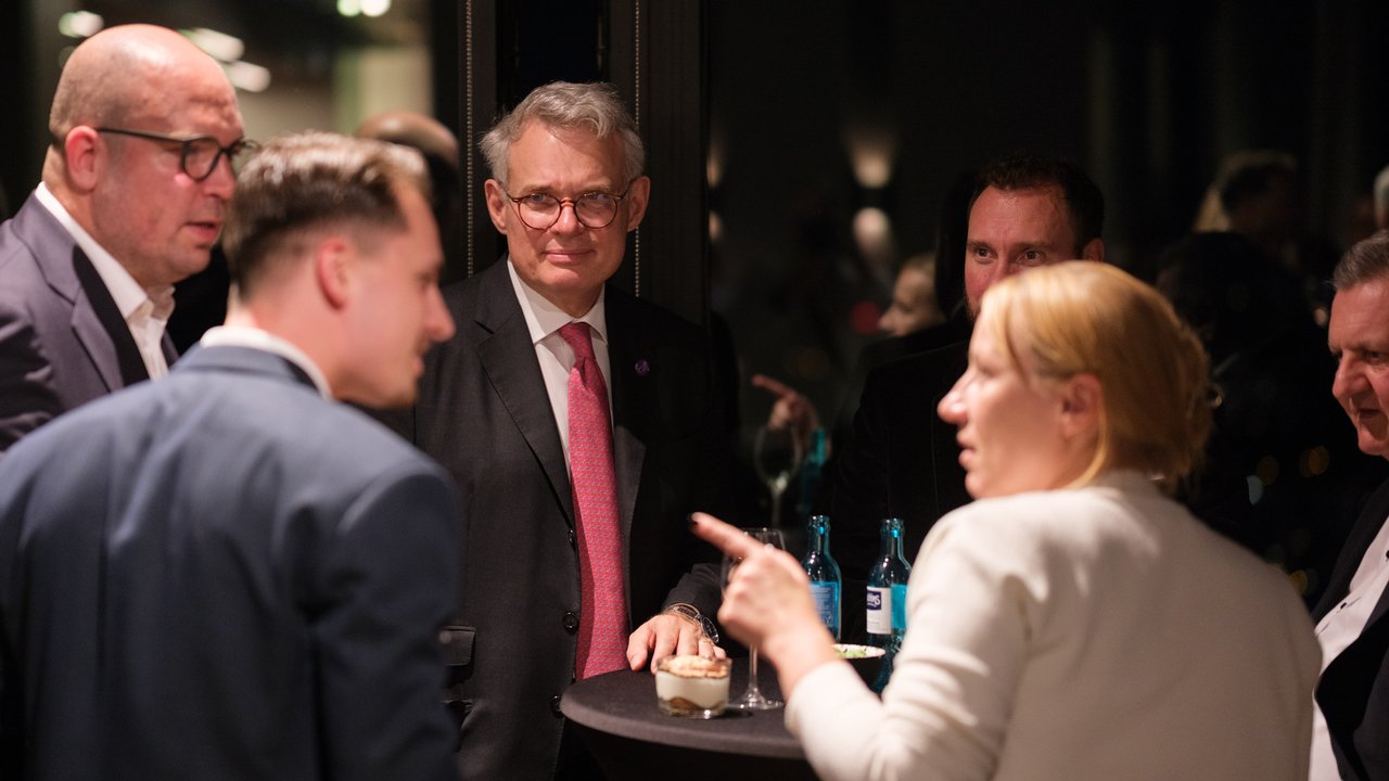 A group of five people engaged in conversation at a table with drinks and snacks in a dimly lit setting.