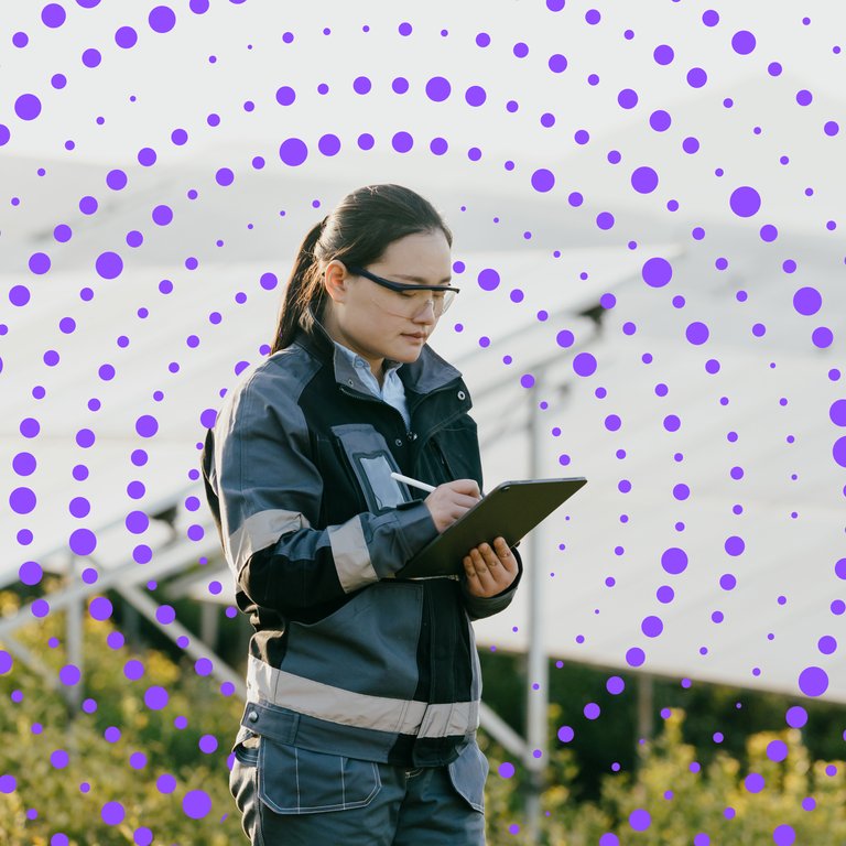 Agricultural worker using a tablet outdoors A person in a work uniform stands outdoors, holding a tablet, with green plants and a white structure in the background.