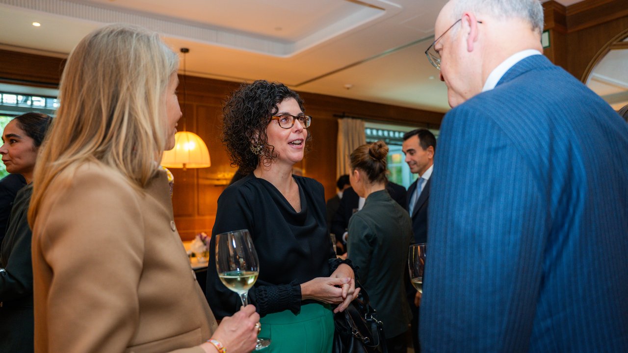 A group of people socializing indoors, with drinks in hand, in a well-lit, elegant setting.