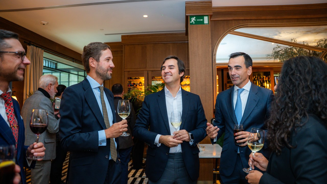 A group of people in formal attire holding drinks in a stylish indoor setting with wooden decor.