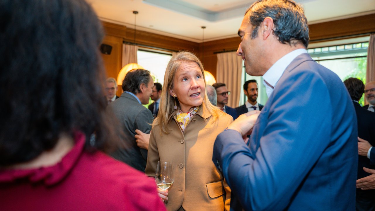 A group of people in formal attire socializing at an indoor event, with drinks in hand and a warm atmosphere.