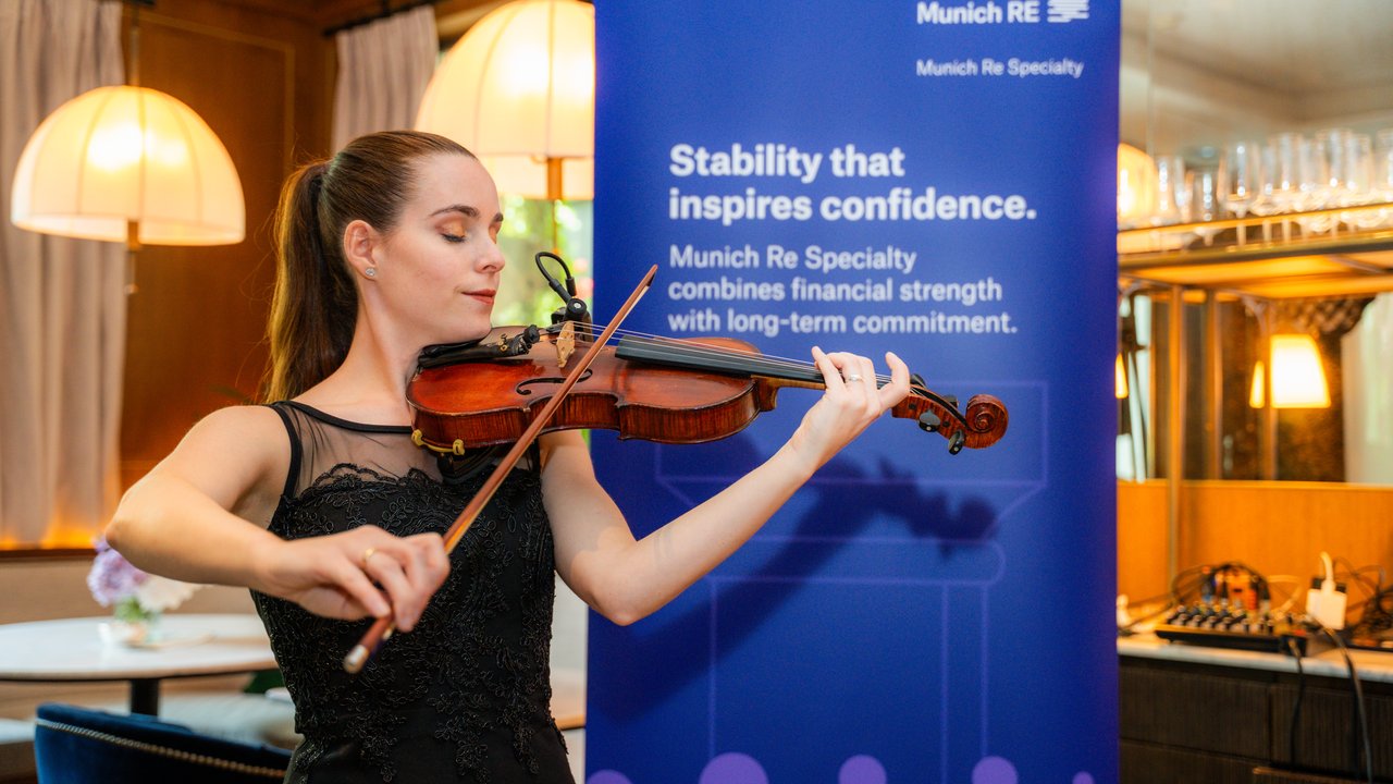 A woman plays the violin in front of a blue banner with Munich Re Specialty branding and text.