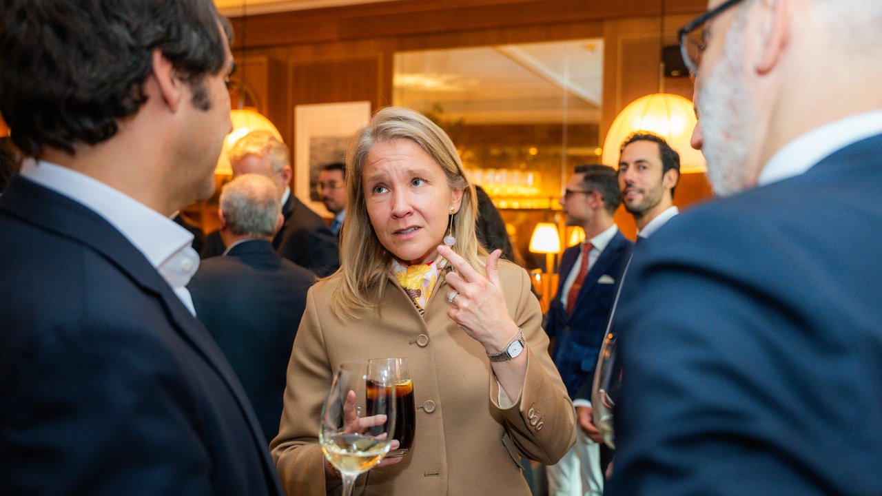 A group of people socializing indoors, with drinks in hand and a warm, elegant atmosphere.