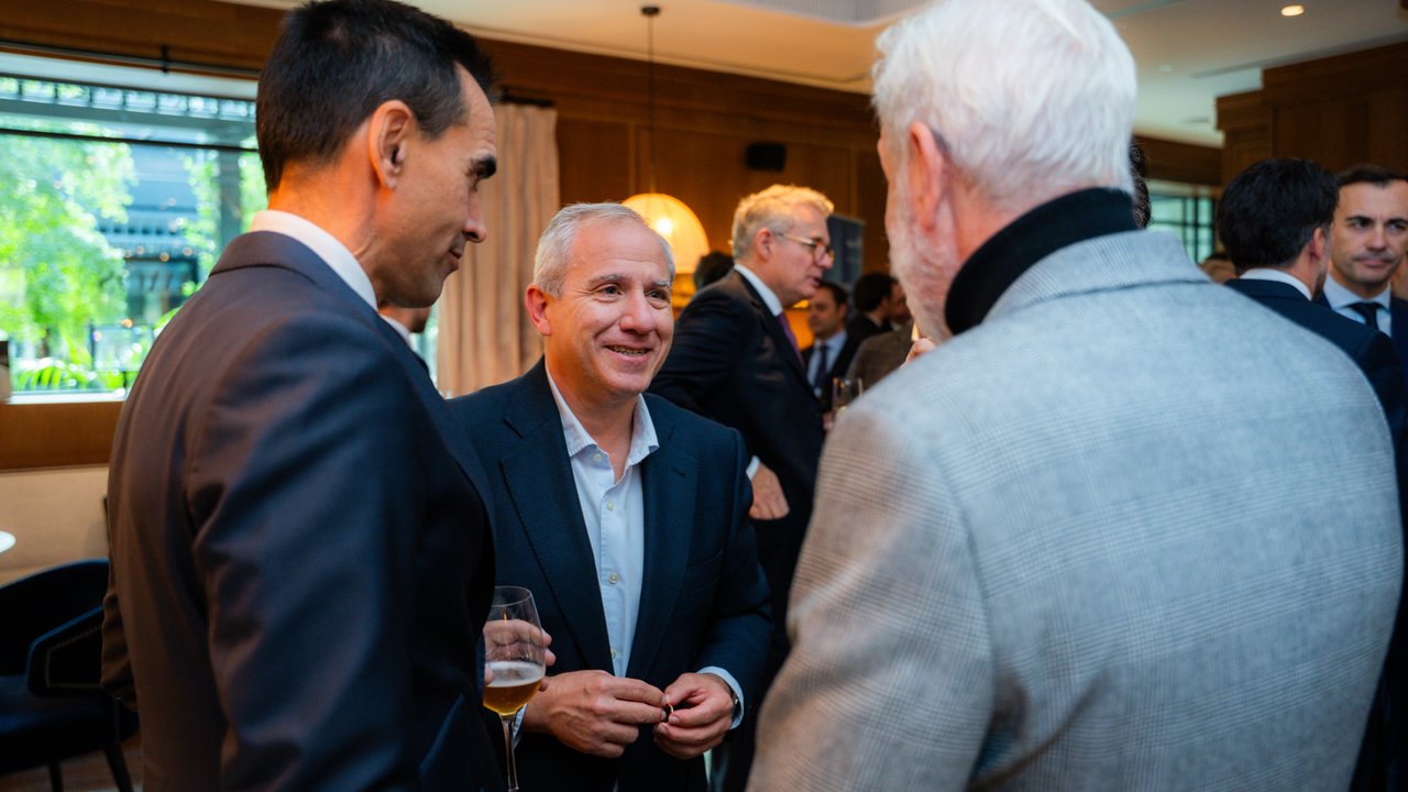 A group of people in formal attire engaged in conversation at a social event, with drinks in hand.