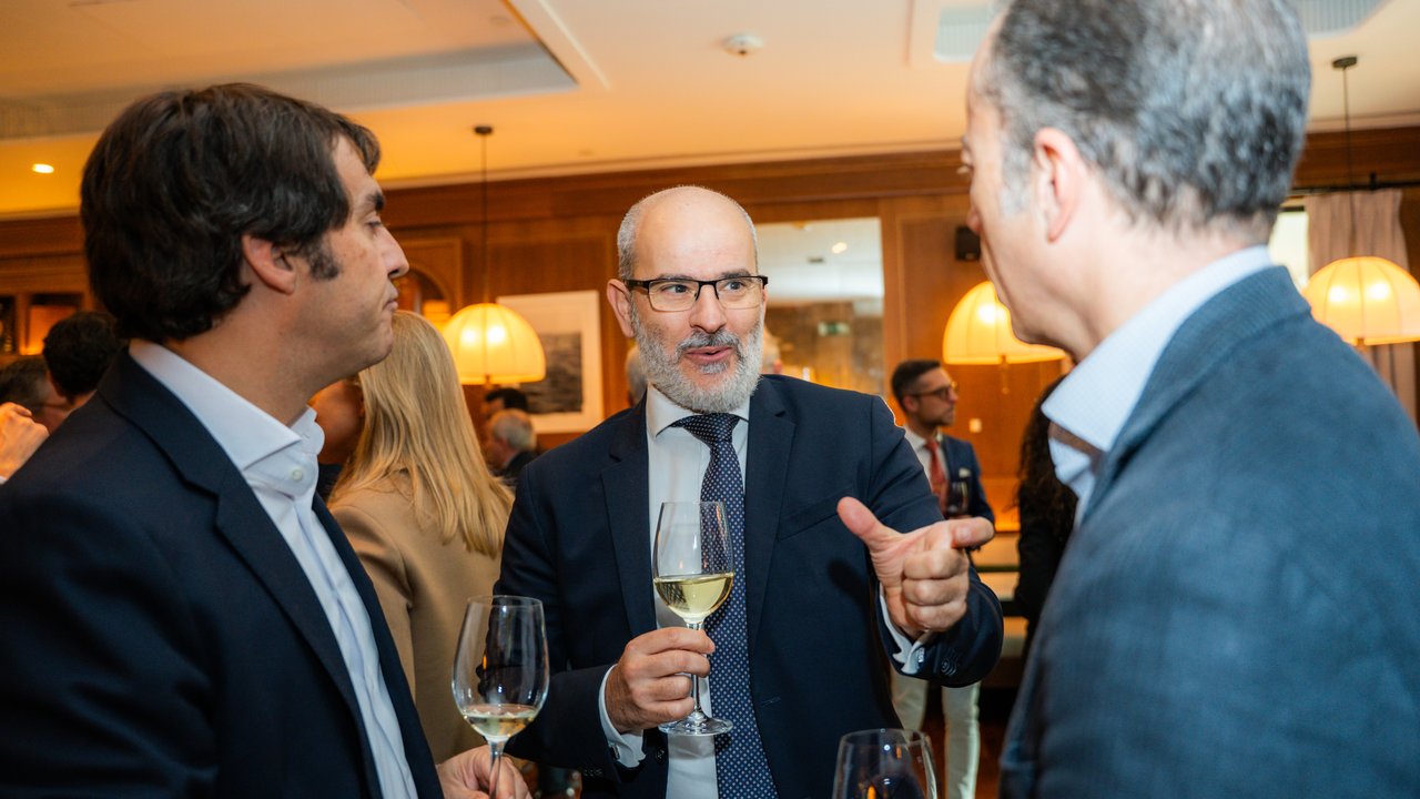 A group of people in formal attire holding glasses at a social gathering in a well-lit indoor setting.
