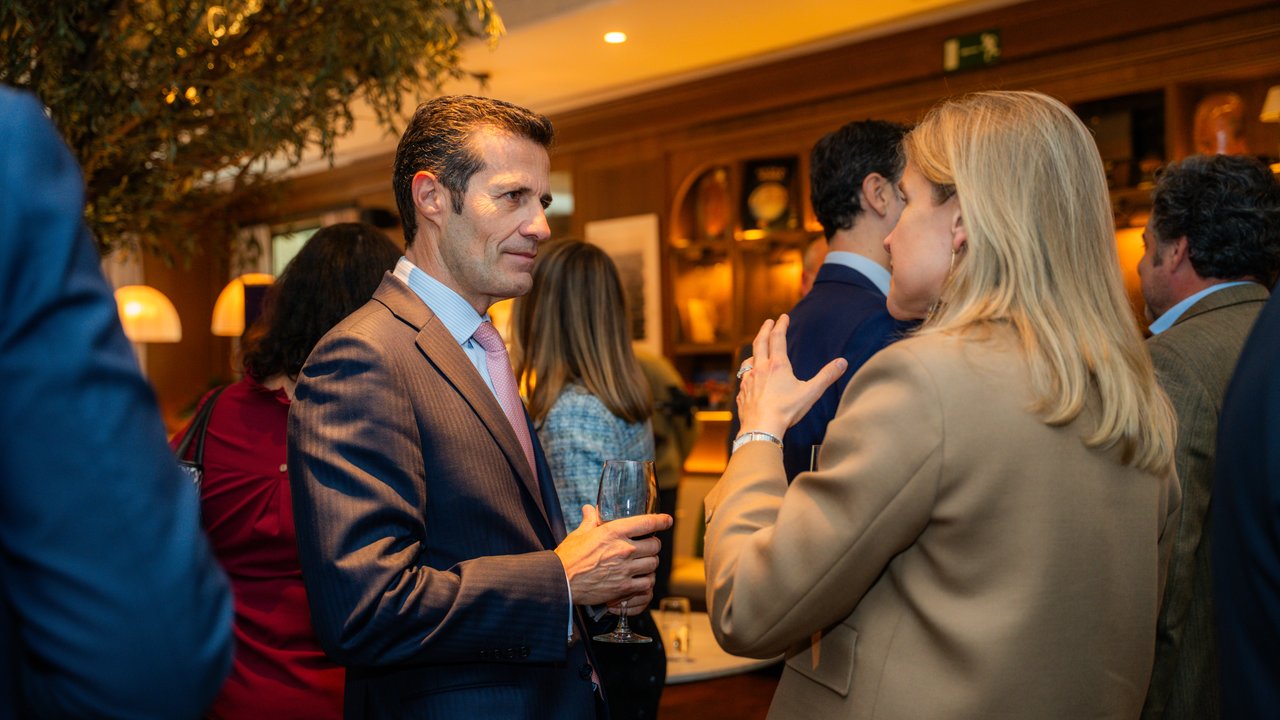 A group of people in formal attire engaged in conversation at a social event, with drinks in hand.