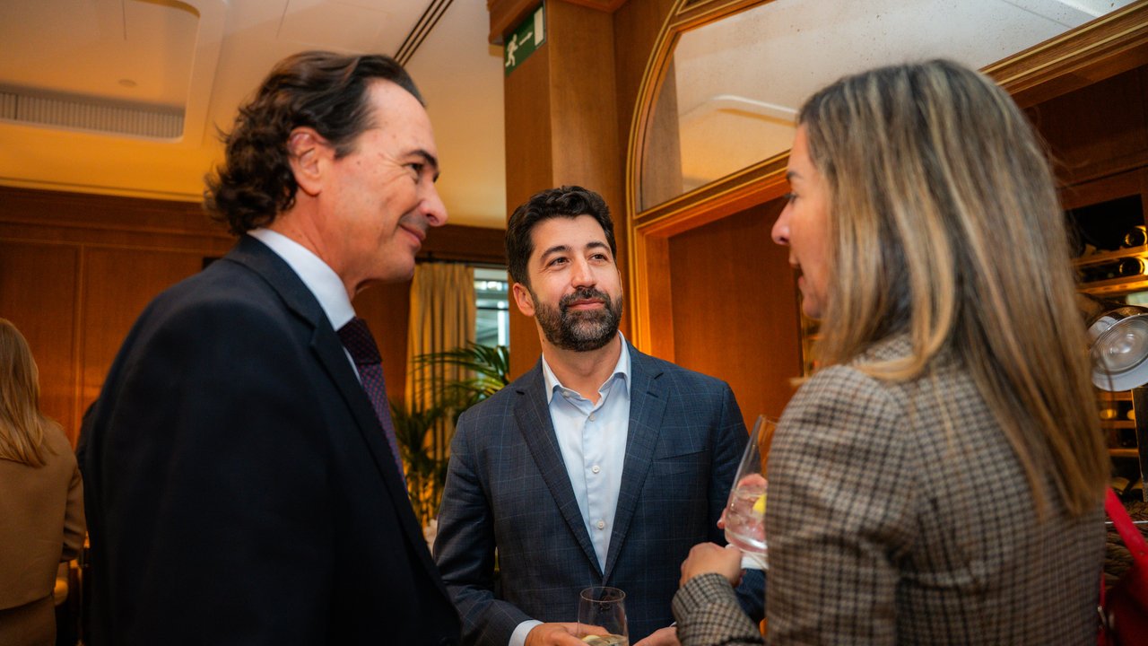 A group of people engaged in conversation at a social event, with drinks in hand and a warm, elegant setting.