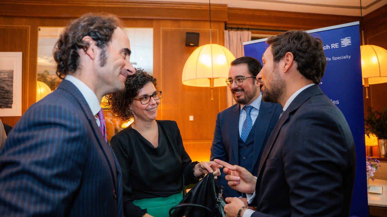 A group of four people engaged in conversation at a social event, with a blue banner in the background.