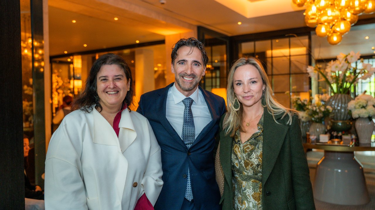 Three people pose together in a well-lit restaurant with decorative lighting and floral arrangements in the background.
