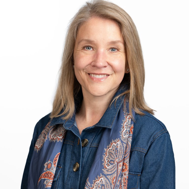Silvi Wompa Sinclair wearing a denim jacket and a patterned scarf stands against a plain white background.