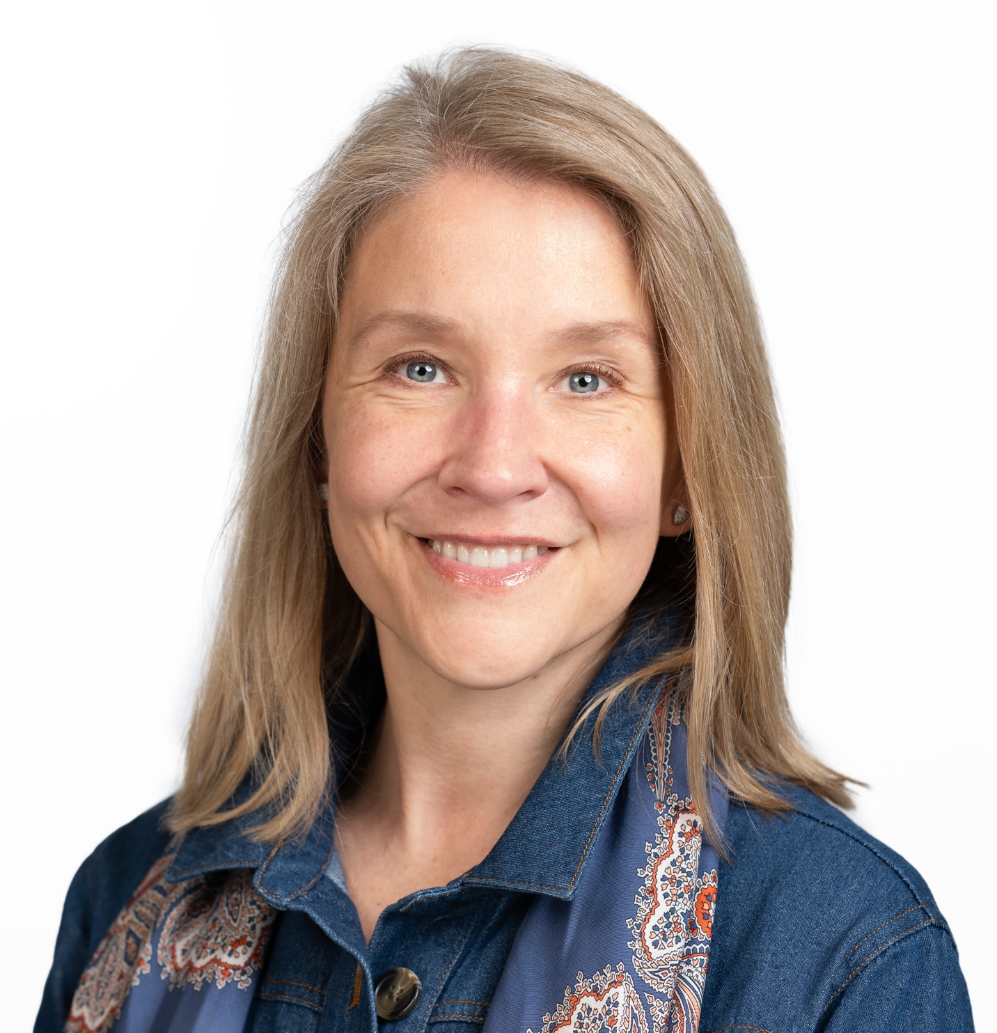 Silvi Wompa Sinclair wearing a denim jacket and a patterned scarf stands against a plain white background.
