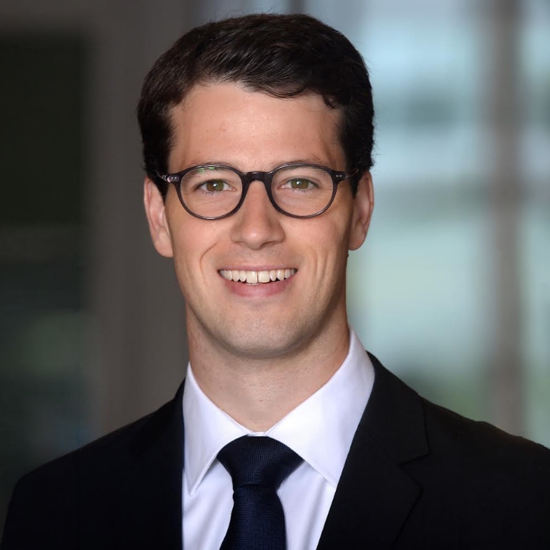 A man in a suit with a blurred face stands against a softly lit background.
