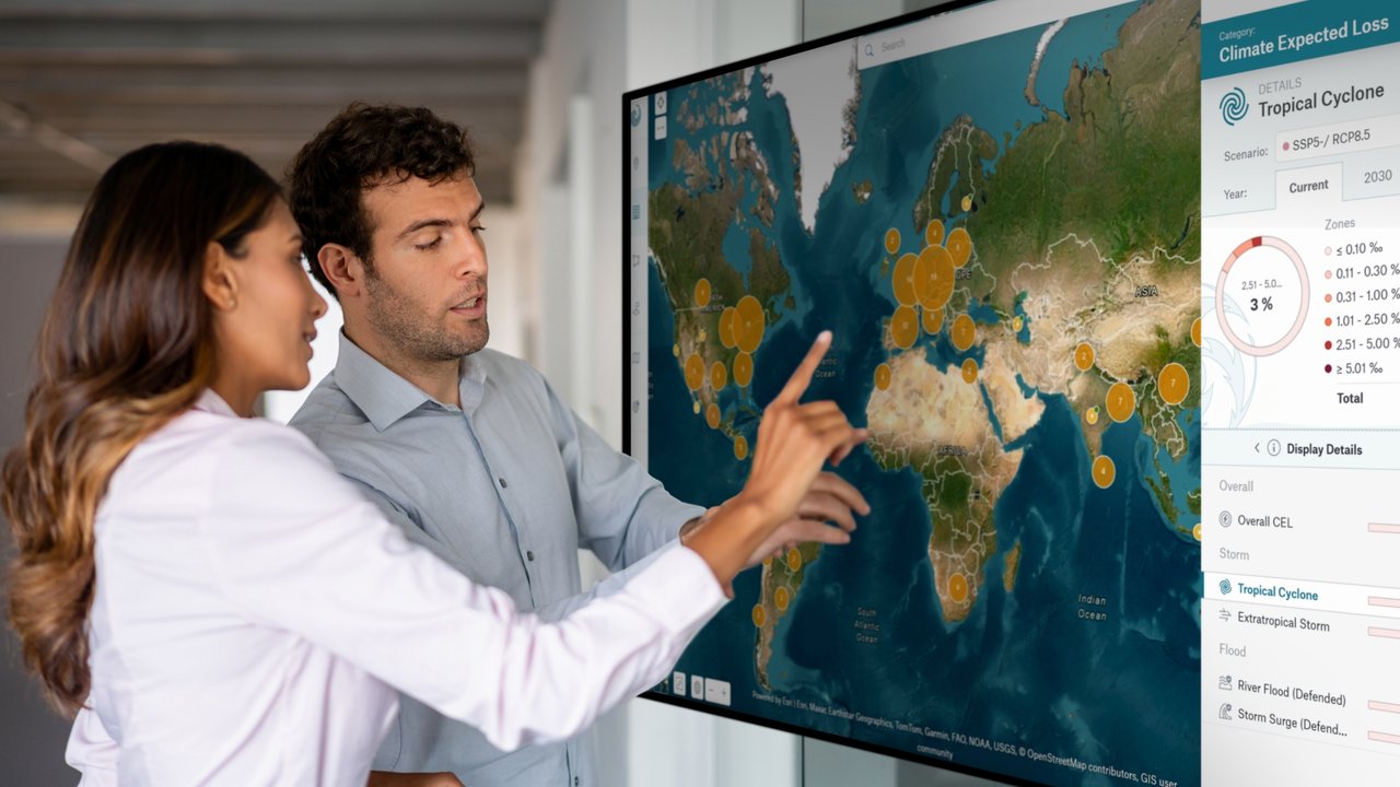 Two people interact with a large screen displaying a world map and climate data related to tropical cyclones.