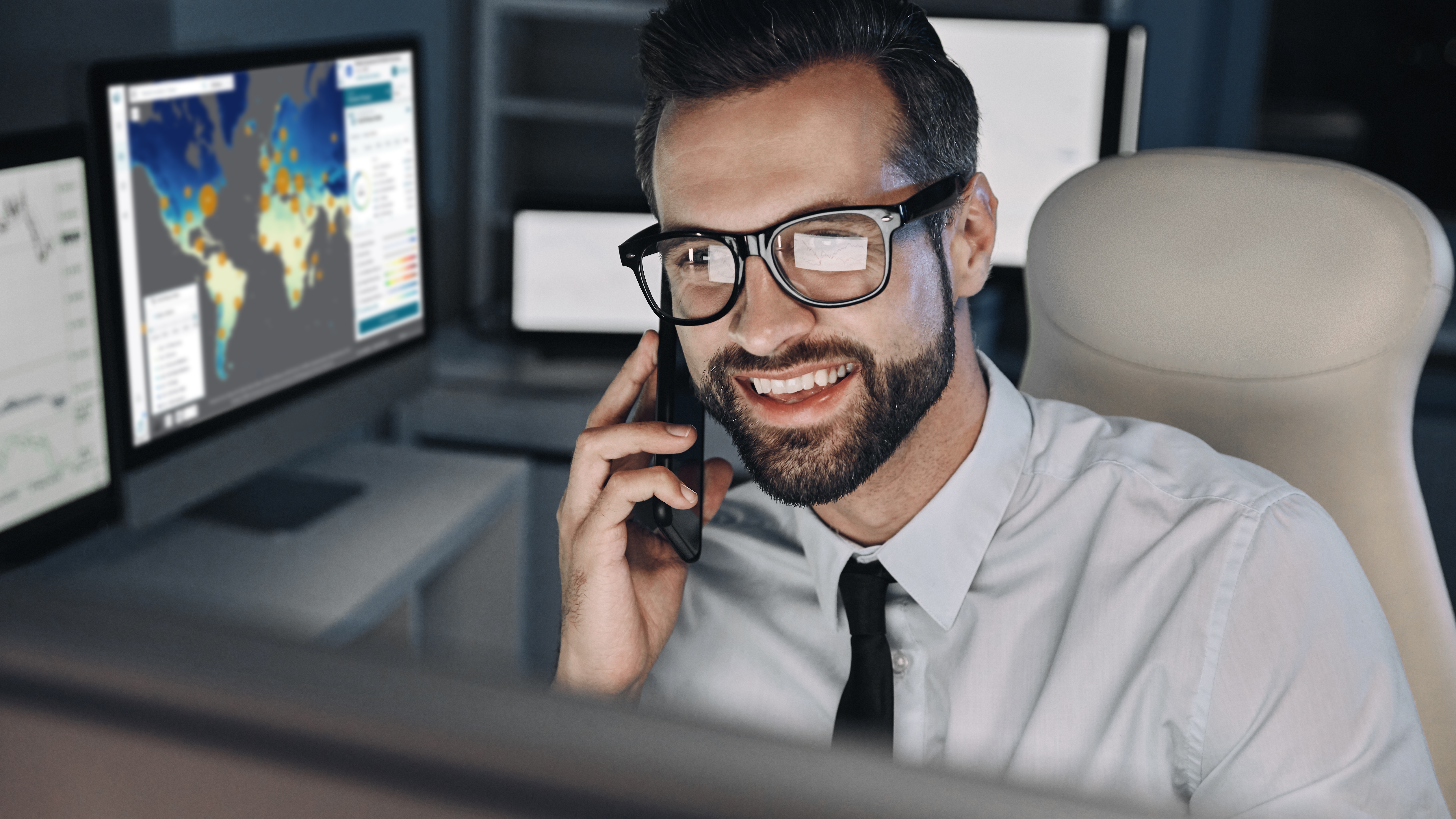 Smiling businessman talking on mobile phone and looking at computer screen in office