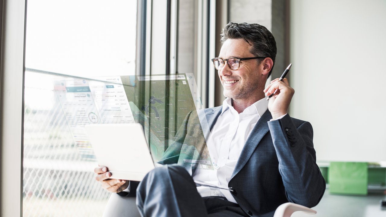 Portrait of smiling businessman with tablet looking through window