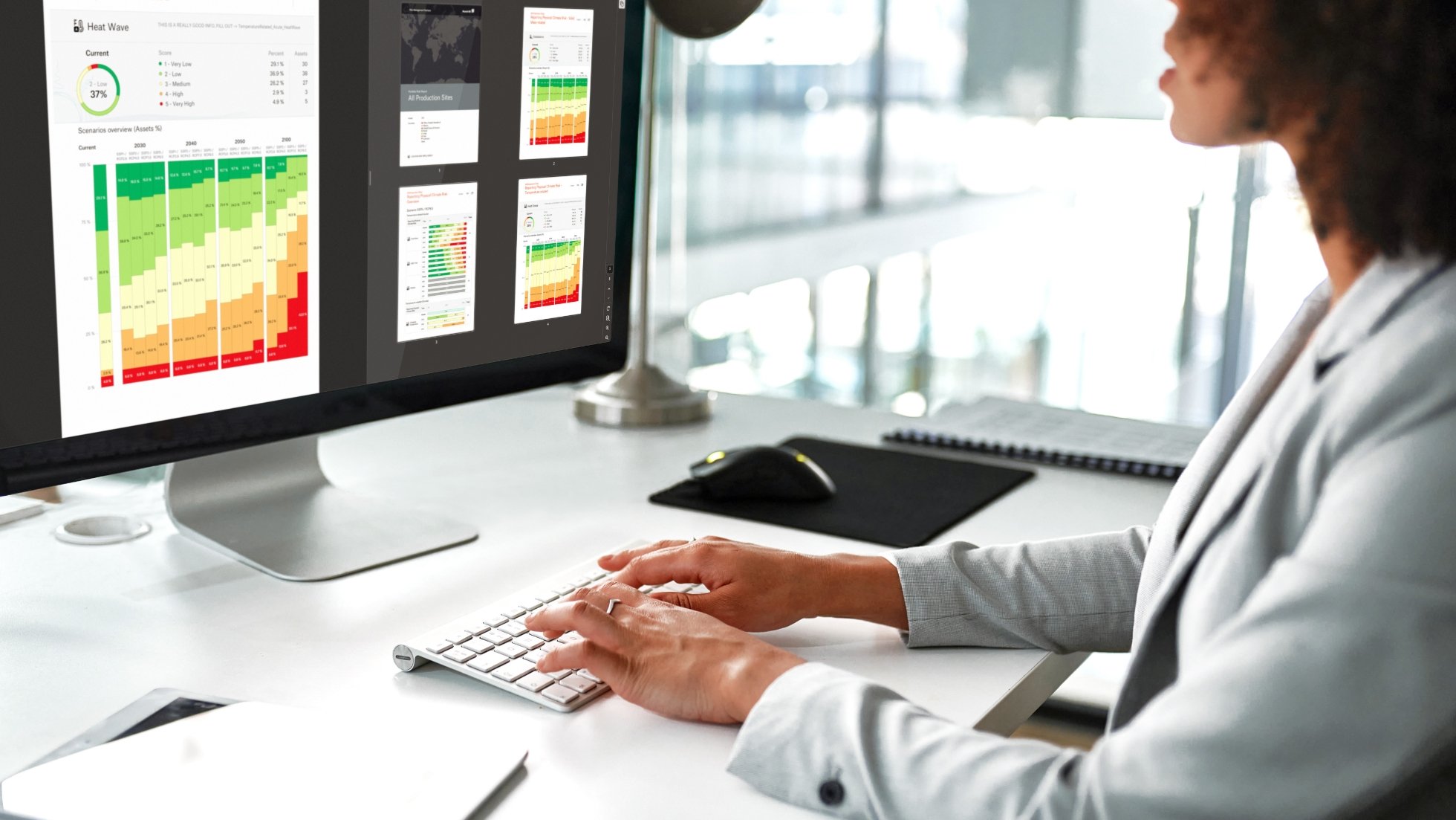 A person in a gray suit types on a keyboard, viewing climate risk data on a computer screen.