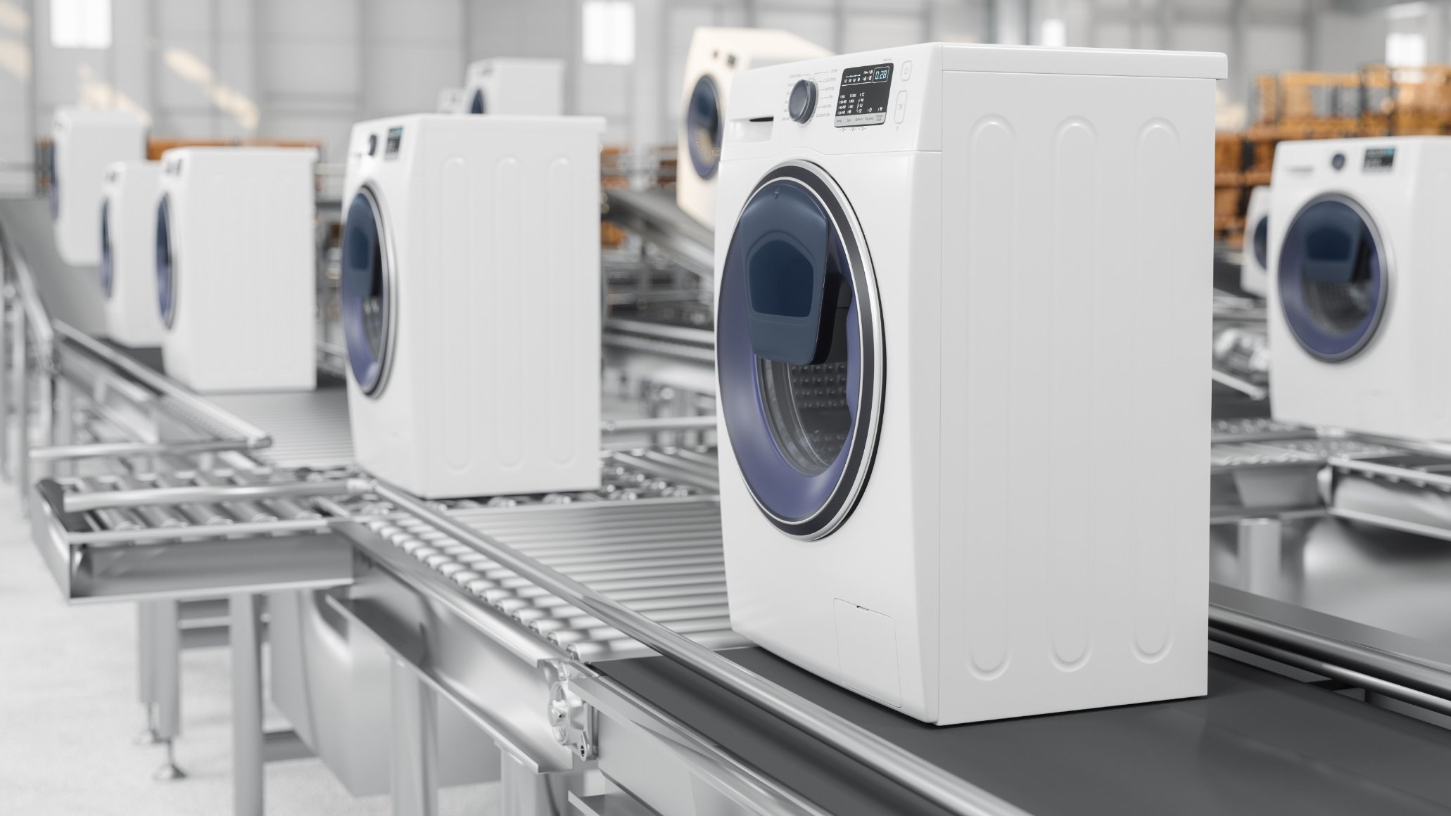 A row of white washing machines on a conveyor belt in a warehouse setting.