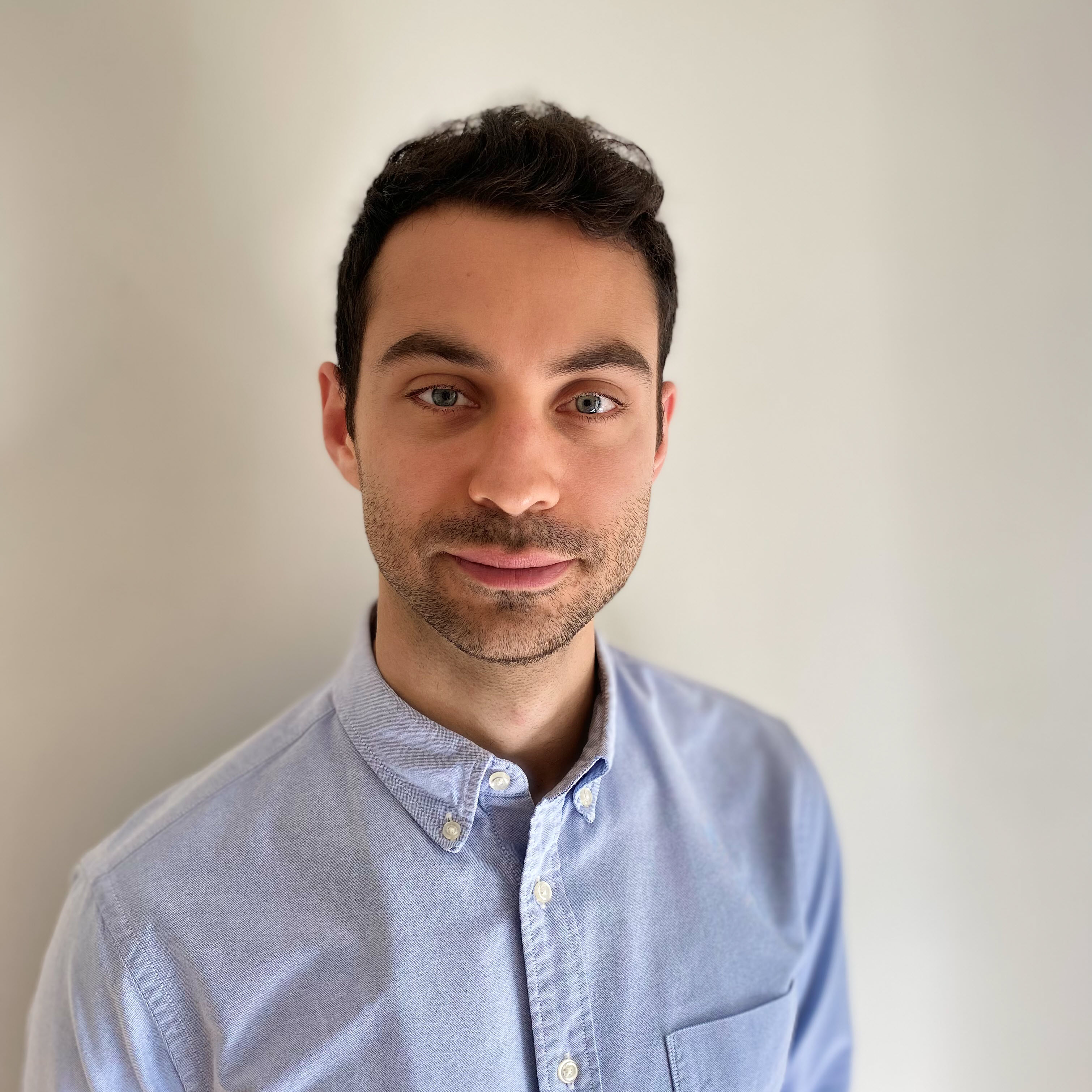 A person wearing a light blue button-up shirt stands against a plain background.